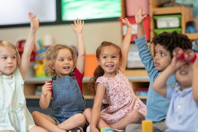 Jeunes enfants assis en cercle au sol, levant la main