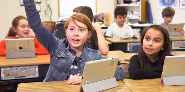 Enfant levant la main dans une classe où les élèves utilisent des tablettes